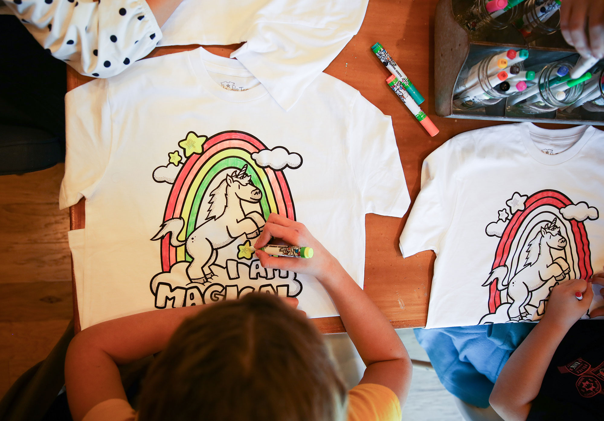 "Photo of kid using fabric markers to color the Doodle Tees 'I Am Magical" design printed on a shirt"